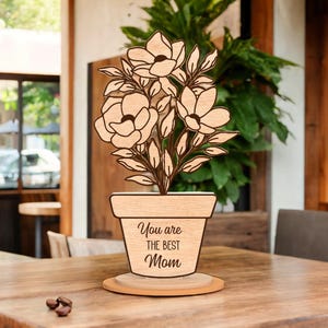 Op de afbeelding: Houten uitsnijding van een plant in een pot met bloemen en de tekst "You are the best Mom" op de pot.