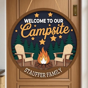 May include: Circular wooden sign with the words "WELCOME TO OUR Campsite" and "STAUFFER FAMILY". The design includes a campfire, two chairs, pine trees, and stars on a dark blue backdrop. A decorative item for a campsite.