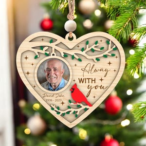 May include: Heart-shaped wooden Christmas ornament featuring a photo of a man, a red cardinal, and the words "Always with you." The ornament includes the name "David John" and the years "1936-2023."