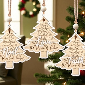 May include: Three wooden Christmas tree decorations shaped like trees, with a light wood grain and white trim. Each has the text "Unto us a child is born" and other religious text. They hang from twine with a wooden bead.
