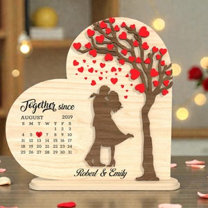 May include: Wooden heart-shaped decorative piece with a calendar for August 2019. Features a tree with red heart-shaped leaves, a couple silhouette, and the names "Robert & Emily". A romantic keepsake.