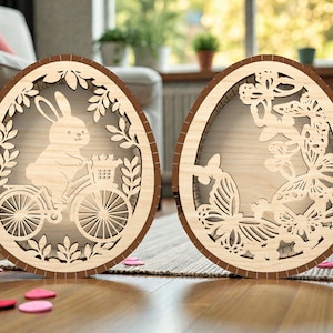 May include: Two wooden Easter egg decorations. One features a bunny riding a bicycle with a basket of flowers, the other has a butterfly design. Both are light brown with a darker brown border.