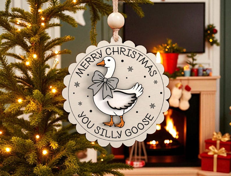 May include: A round, wooden Christmas ornament with a scalloped edge. The ornament features a cartoon goose wearing a bow tie, with the text "MERRY CHRISTMAS YOU SILLY GOOSE" around the edge. The ornament is hanging from a string.