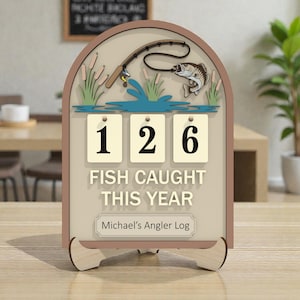 Puede incluir: Un letrero de madera con temática de pesca con un marco marrón, que presenta una caña de pescar, un pez y el texto "FISH CAUGHT THIS YEAR". El letrero muestra el número "126" e incluye el texto "Michael's Angler Log".