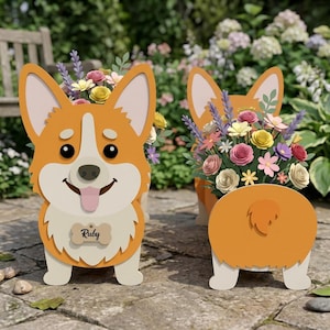 May include: Two orange and white corgi-shaped planters filled with colorful paper flowers. The corgis have a smiling face, a pink tongue, and a bone-shaped tag that says "Ruby". The planters are on a stone surface.