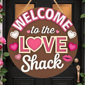 May include: A round, brown wooden sign with the words "WELCOME to the LOVE Shack" in white and pink lettering. The sign features heart and lip accents. A rope is attached for hanging. Roses frame the door.