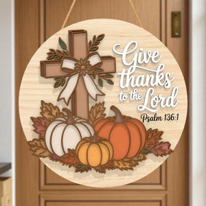 May include: Round wooden sign with a cross, pumpkins, and fall leaves. The sign reads "Give thanks to the Lord" with "Psalm 136:1" below. The sign is hanging on a wooden door.