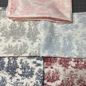May include: Assortment of fabric pieces featuring a classic toile de Jouy pattern. The fabrics display scenes of figures and landscapes in various colors, including pink, gray, blue, navy, and burgundy, against a white background. The fabrics are folded and stacked.