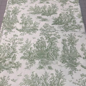 May include: A rectangular fabric with a white background and a green toile pattern. The pattern depicts scenes of people, trees, and birds. The fabric is likely used for home decor or crafting projects.