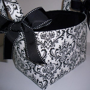 May include: A black and white damask fabric storage basket with black ribbon handles and a black bow. The basket has a black fabric lining.