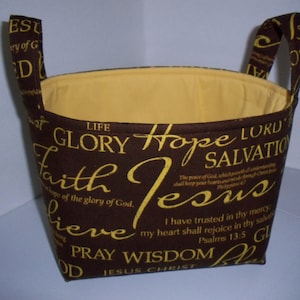 May include: A brown fabric storage basket with yellow lettering. The lettering includes words like "Life", "Glory", "Hope", "Lord", "Salvation", "Faith", "Jesus", "Pray", "Wisdom", and "Jesus Christ".