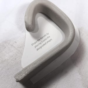 Curved mug handle formed with pottery template, handbuilt and shaped for DIY ceramic cup, beginner pottery tool for round mug projects.