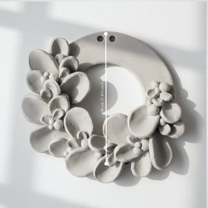 Unglazed ceramic wreath with sculpted leaves arranged on a round base, showing details of handmade pottery and ceramic wreath design before firing.
