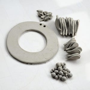 Work-in-progress shot of clay wreath base, leaves, and berries laid out with holes for hanging, demonstrating slab-building pottery kit components and pottery tools.