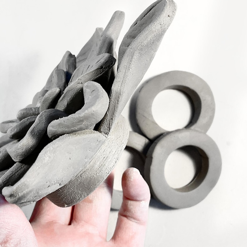 Hand holding clay flowerswith a ring-shaped base.
