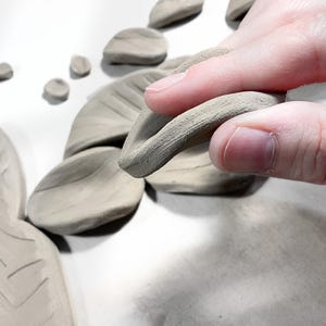Hands cutting clay flowers from a ceramic template sheet, demonstrating how to use printable pottery templates with basic pottery tools and air dry clay.