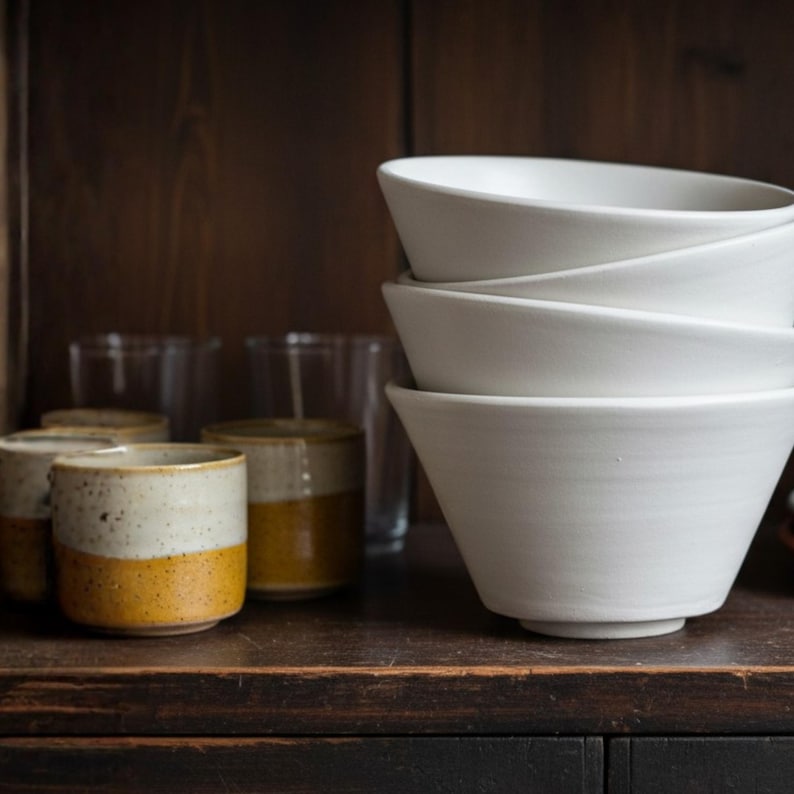 Stacked bowls on rustic wooden shelf, handmade and fired, for functional ceramic storage. Modern and minimal pottery style.
