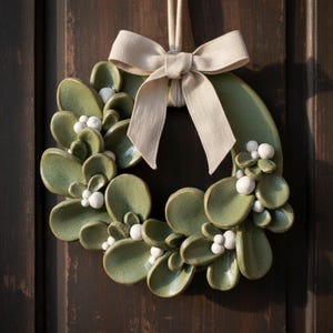 Handmade ceramic wreath with green glazed leaves and ribbon, hanging as a door wreath, showcasing Christmas pottery and handmade ceramics.