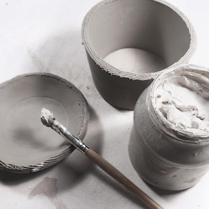 Pottery workspace with round clay mug in progress, DIY pottery template, slab-building method, clay and brush ready for handbuilt mug crafting.