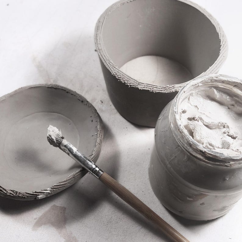 Pottery workspace with round clay mug in progress, DIY pottery template, slab-building method, clay and brush ready for handbuilt mug crafting.