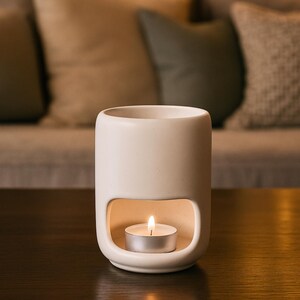 Fired and glazed ceramic oil burner, minimalist shape, perfect for essential oils or soy wax melts, in use in a cozy living room.