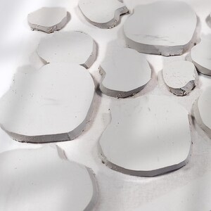May include: A collection of irregularly shaped, light gray, stone-like objects. The objects have a smooth, flat surface and a darker gray edge. The arrangement suggests a decorative or artistic theme, possibly for home decor or craft projects.