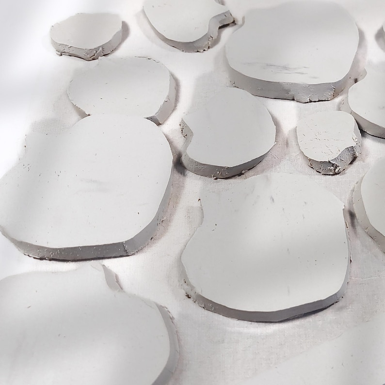 May include: A collection of irregularly shaped, light gray, stone-like objects. The objects have a smooth, flat surface and a darker gray edge. The arrangement suggests a decorative or artistic theme, possibly for home decor or craft projects.
