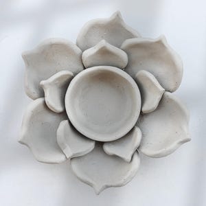 May include: A gray, handmade, ceramic flower-shaped dish. The dish has a central bowl surrounded by petal-shaped sections. The petals and bowl have a matte finish. The dish is likely used for decorative purposes or as a small serving piece.