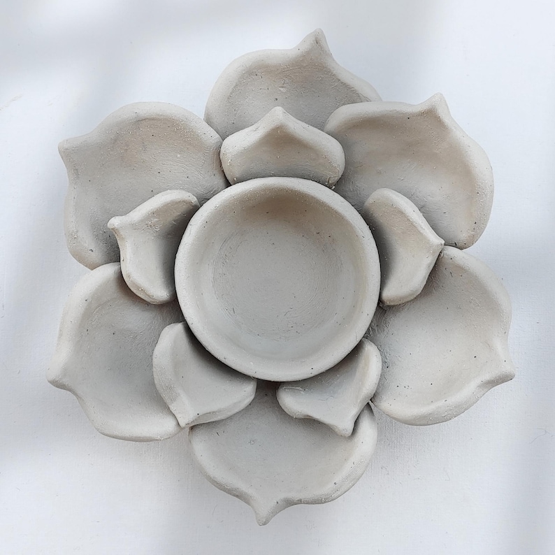 May include: A gray, handmade, ceramic flower-shaped dish. The dish has a central bowl surrounded by petal-shaped sections. The petals and bowl have a matte finish. The dish is likely used for decorative purposes or as a small serving piece.