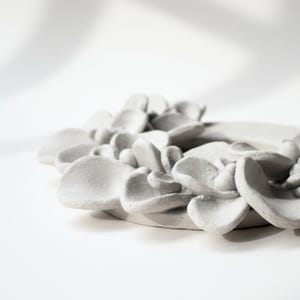 Unglazed ceramic wreath with sculpted leaves from a side view, showing details of handmade pottery and ceramic wreath design before firing.