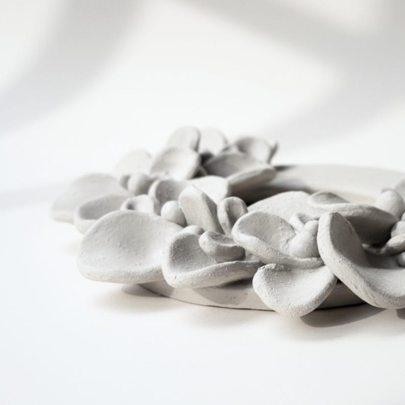 Unglazed ceramic wreath with sculpted leaves from a side view, showing details of handmade pottery and ceramic wreath design before firing.