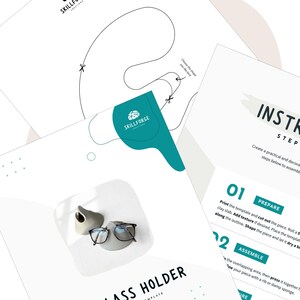 May include: A collection of white paper templates with instructions for a glass holder, featuring a teal logo and a pair of eyeglasses. The instructions include steps for preparing and assembling the holder. A small gray ceramic holder is also visible.