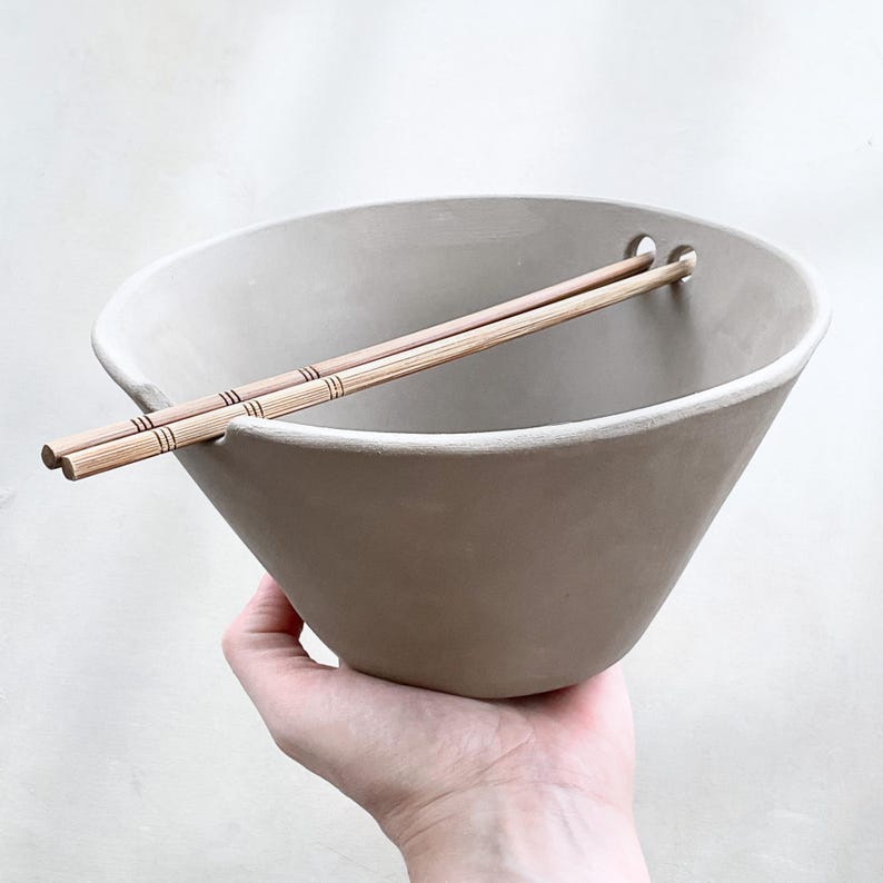 Hand holding leather-hard bowl with chopsticks resting in groove, classic noodle or ramen style with wabi sabi detail. Made by using a ramen bowl pottery template.