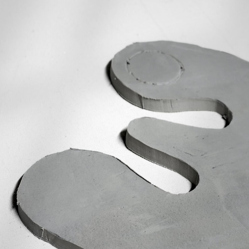 May include: Two gray, abstract, interlocking shapes with rounded edges and a circular indentation. The shapes are on a white background, creating a minimalist and modern aesthetic. The objects appear to be made of a solid, possibly manufactured material.