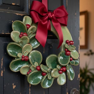Finished green Christmas pottery wreath with red berries and bow, used as a festive door wreath, highlighting handmade ceramics and Christmas pottery decor.