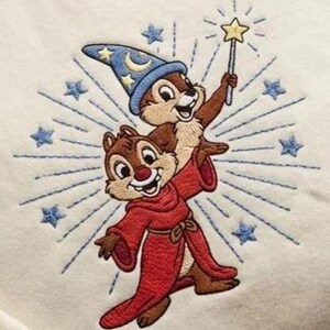 May include: Embroidered design featuring two cartoon chipmunks. One chipmunk wears a red robe and the other a blue wizard hat with stars and a crescent moon. The chipmunk in the hat holds a star-tipped wand. Blue starburst and stars surround the chipmunks.