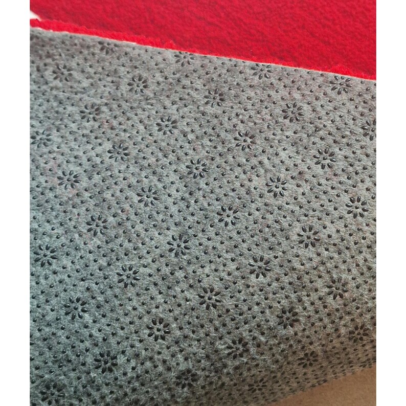 May include: Close-up of a red and gray rug. The top portion is a solid, vibrant red. The bottom portion is gray with a pattern of small, black, flower-shaped anti-slip grips.