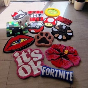 May include: A collection of colorful, decorative rugs in various shapes and designs. The rugs include a red lip, a paw print, a flower, a mushroom, and the text "Fortnite". A white cat is standing on the rugs.