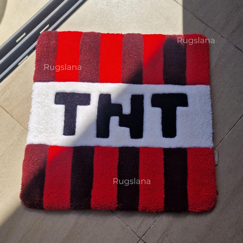 May include: A rectangular rug with a TNT design. The rug features alternating red and black vertical stripes with a white central section. The letters "TNT" are displayed in black. The brand name "Rugslana" is visible.