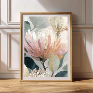 Puede incluir: Una impresión artística enmarcada que presenta una pintura de acuarela de flores de protea en tonos rosa, melocotón y blanco, sobre un fondo de hojas verdes y grises apagados. La obra de arte se muestra en un marco de madera clara.