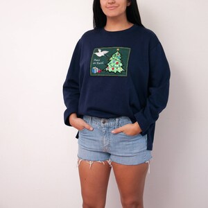May include: A navy blue sweatshirt with a green embroidered Christmas tree and a white dove with the text "Peace on Earth".