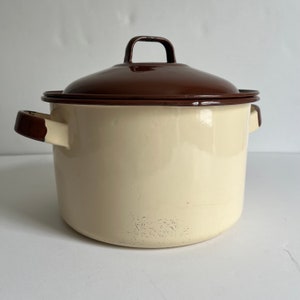 May include: A white enamel pot with a brown lid and brown handles. The pot has a vintage look and is perfect for cooking.