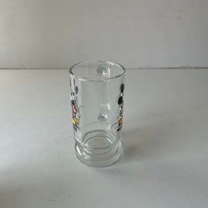 May include: A clear glass mug with a Mickey Mouse and Minnie Mouse design. The mug has a handle and a rounded base.