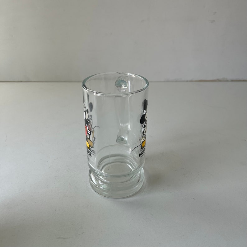 May include: A clear glass mug with a Mickey Mouse and Minnie Mouse design. The mug has a handle and a rounded base.