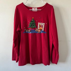 May include: Red long-sleeved shirt with a Christmas tree and fireplace design made of sequins and beads.