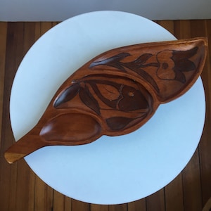 May include: A wooden serving tray shaped like a leaf with carved floral designs and three separate compartments. The tray is brown and has a natural wood finish.