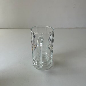 May include: A clear glass mug with a handle. The mug has a black and white cartoon image of Mickey Mouse and Minnie Mouse on the side.