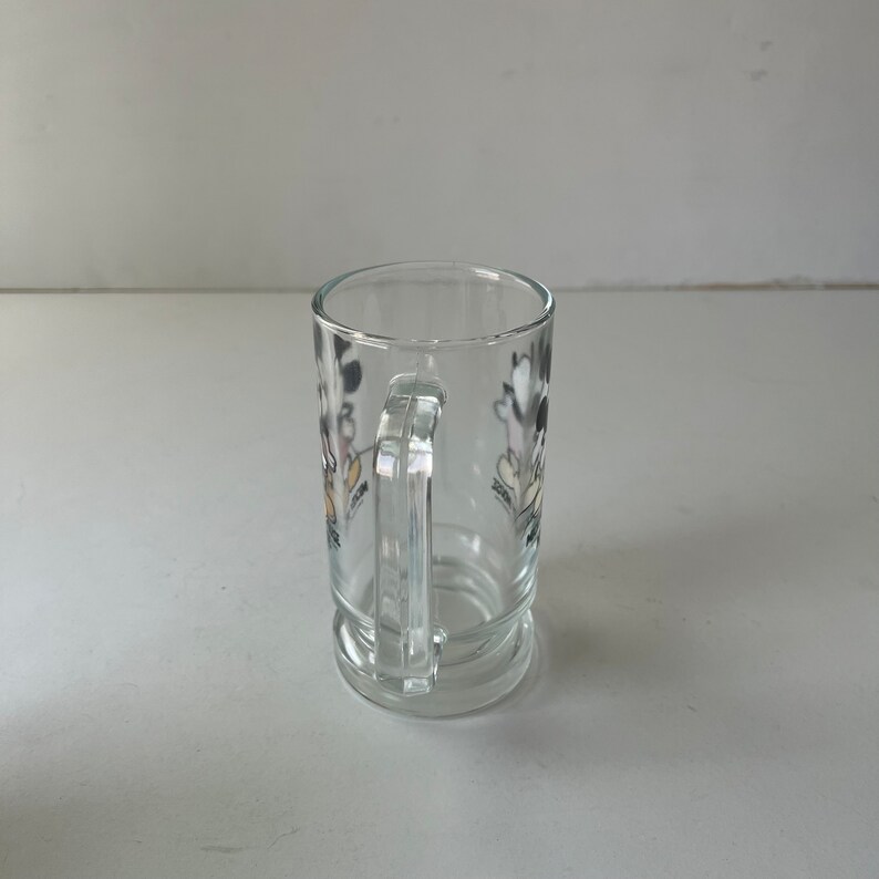 May include: A clear glass mug with a handle. The mug has a black and white cartoon image of Mickey Mouse and Minnie Mouse on the side.
