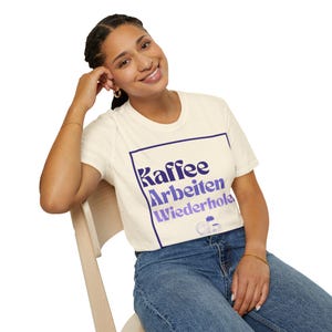 May include: A white t-shirt with a purple and blue graphic that says "Kaffee Arbeiten Wiederhole" in a retro font.