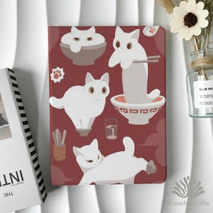 May include: A red tablet case featuring white cartoon cats interacting with ramen bowls, chopsticks, and paw prints. The design includes a glass of water and a container of chopsticks. The case has a glossy finish.